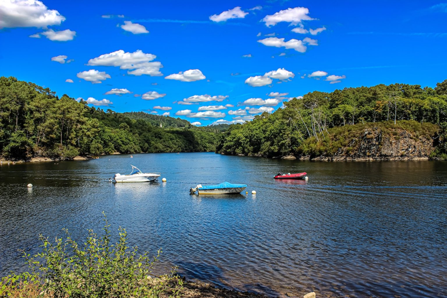 Les 7 plus beaux lacs de montagne pour se rafraîchir en été three boats floating on top of a lake surrounded by trees