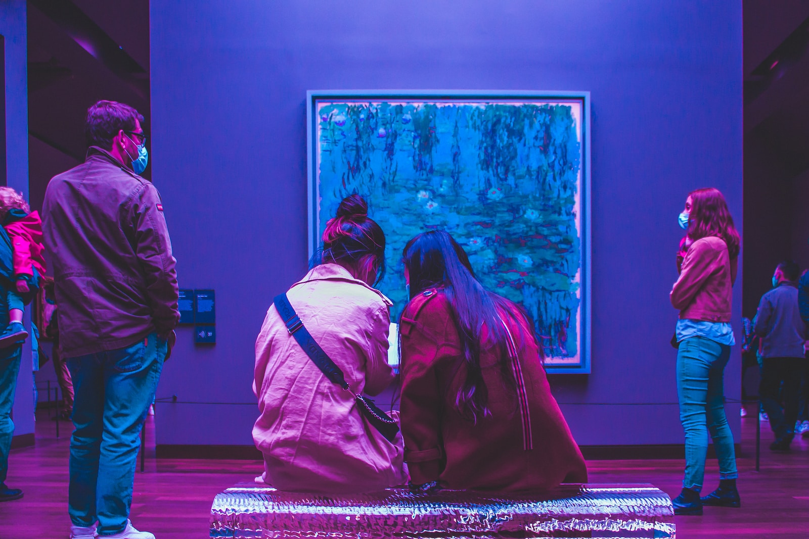 two people sitting on a bench in front of a painting