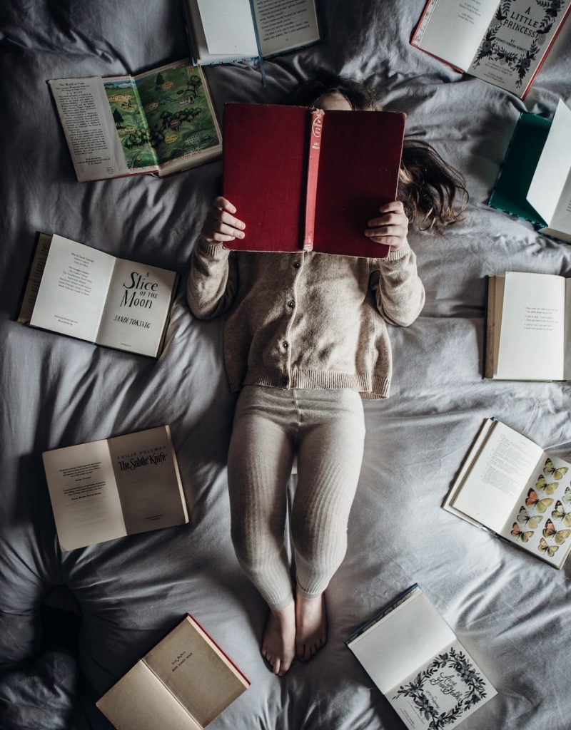 a little girl laying on a bed with lots of books