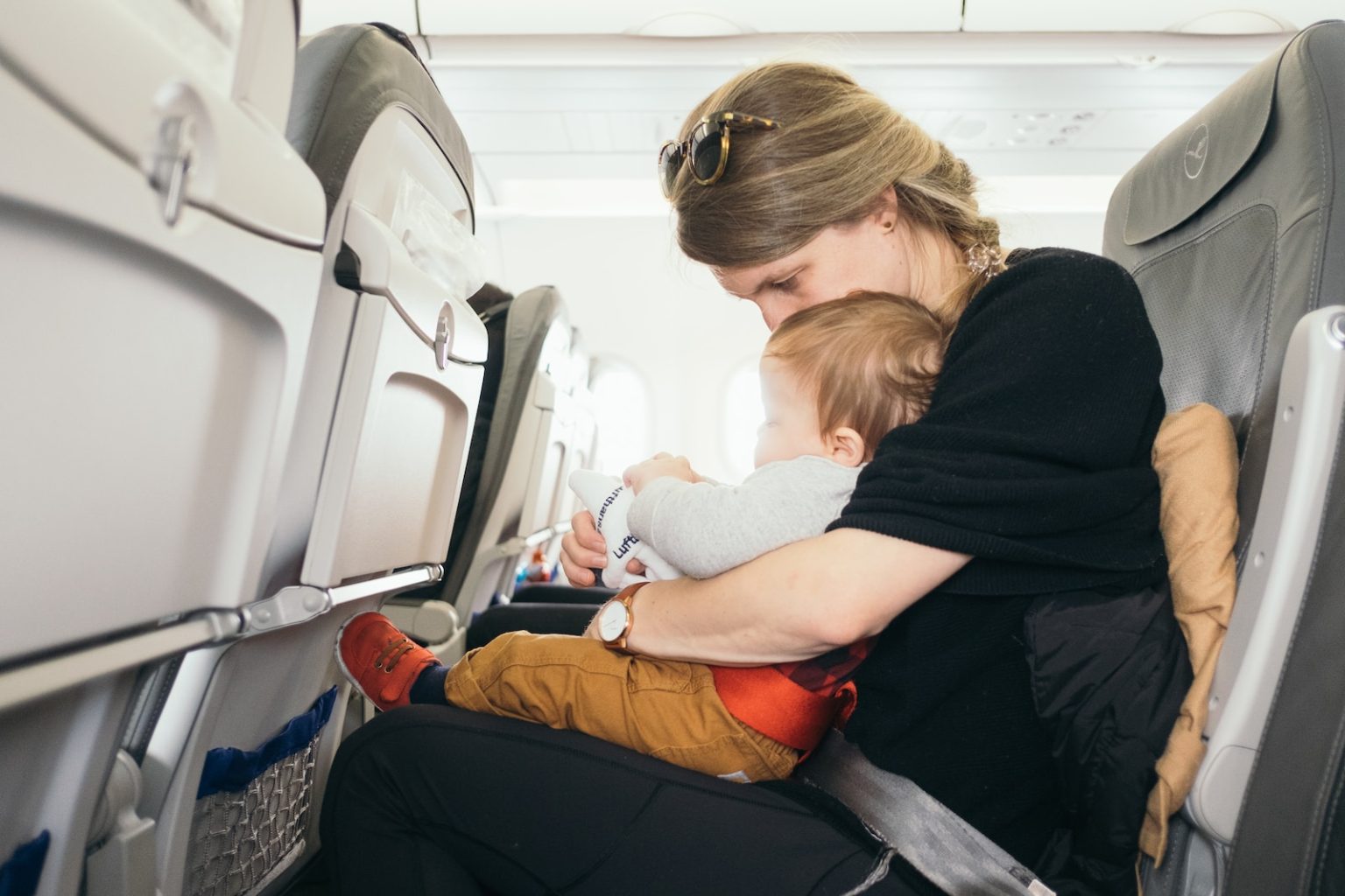 Comment voyager en avion avec un nourrisson ou un jeune enfant ? woman carrying baby while sitting on gray seat
