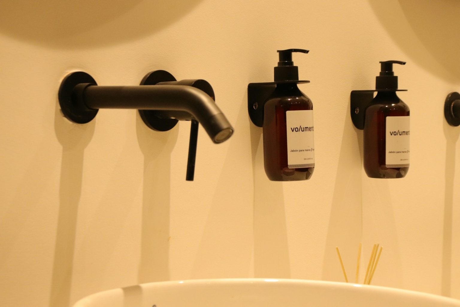 a bathroom sink with three soap dispensers on the wall
